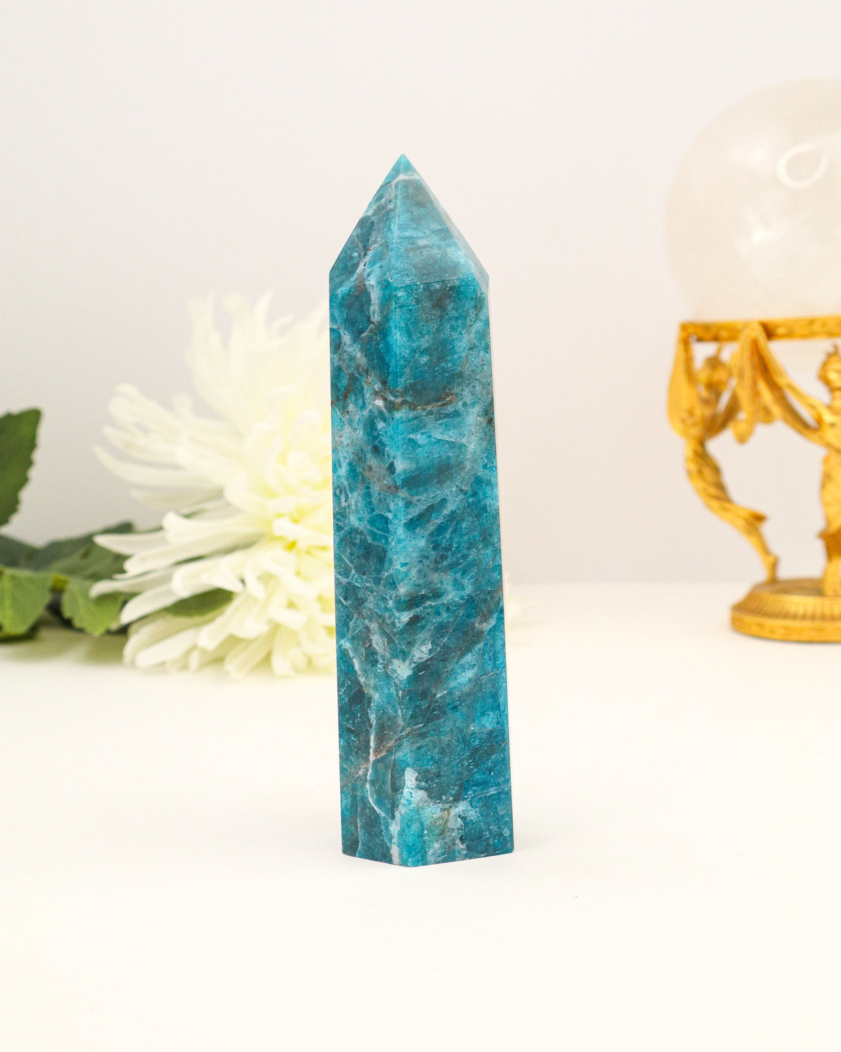Polished Blue Apatite crystal tower with vibrant ocean-blue colouring photographed on a cream background with floral styling.