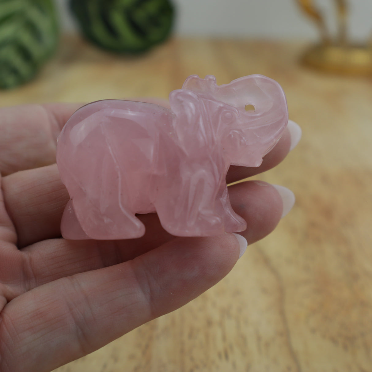 Rose quartz elephant carving displayed on wooden surface beside ruler showing size