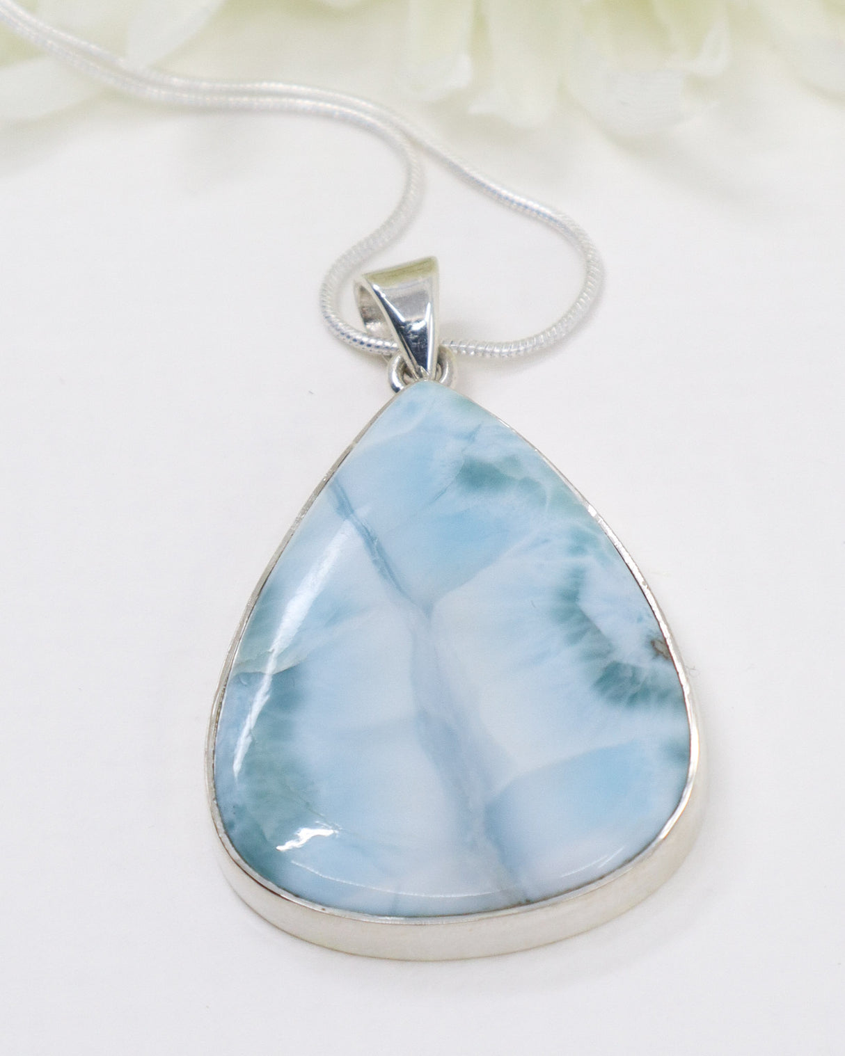 Teardrop-shaped larimar pendant with marbled blue and white design on a beige background