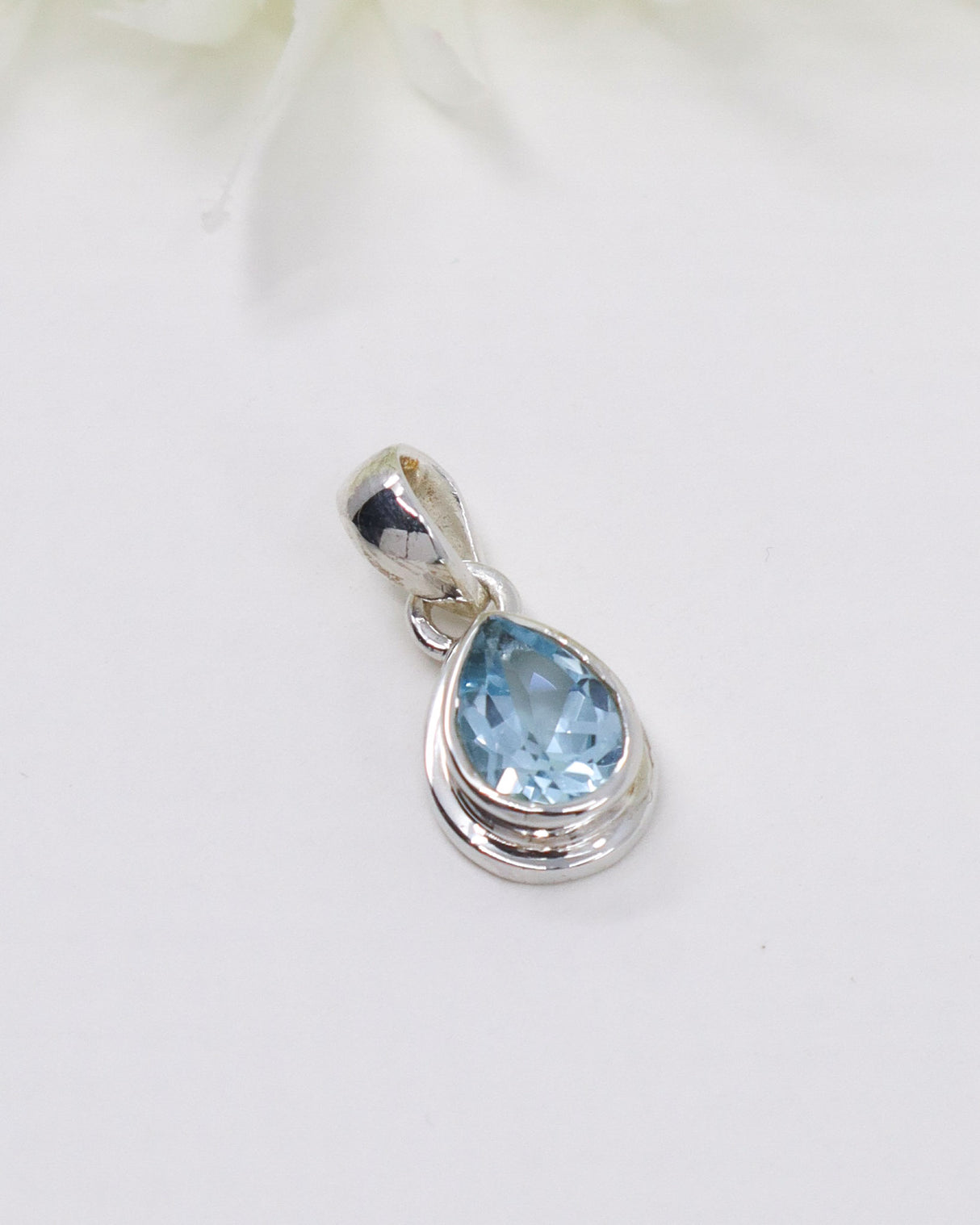 Pear-cut Blue Topaz sterling silver pendant with faceted light blue gemstone on a soft cream background by Inspired By 3 Australia.