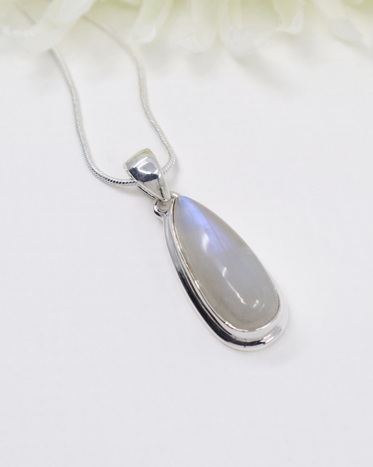 Rainbow Moonstone sterling silver pendant with soft blue flash displayed on silver chain against elegant white background.