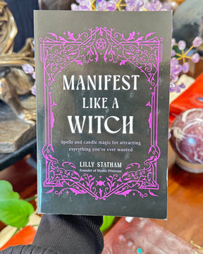 Manifest Like A Witch book by Lilly Statham featuring black cover with pink gothic design and candle magic manifestation subtitle