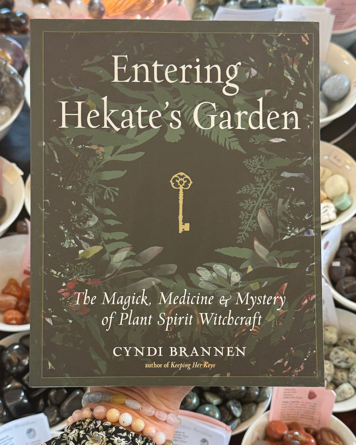 Entering Hekate’s Garden by Cyndi Brannen, herbal witchcraft book featuring mystical botanical illustrations, sacred green foliage, golden Hekate key and plant spirit magick.