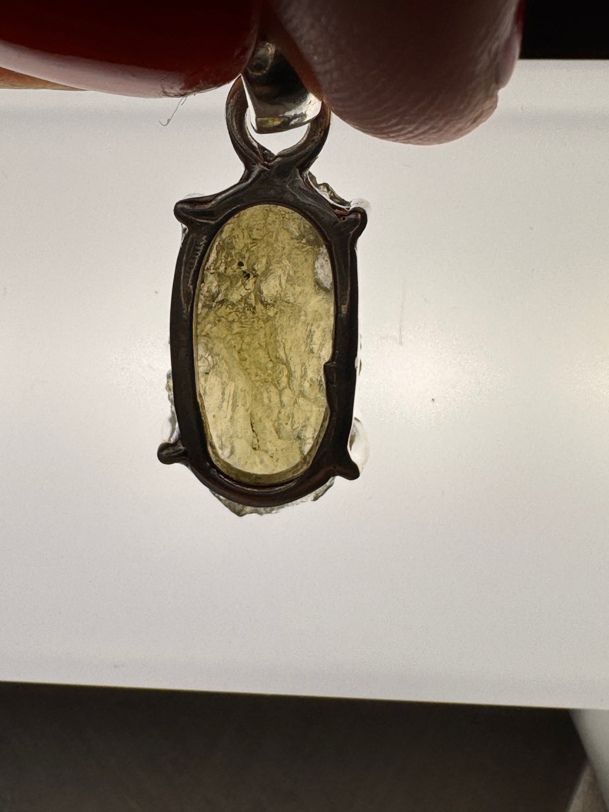 Moldavite pendant backlit to show internal clarity and ridged texture, 2.28g weight