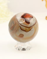 Polished Polychrome Jasper crystal sphere with natural earthy brown, cream and terracotta patterns displayed on a clear stand against a soft cream background.