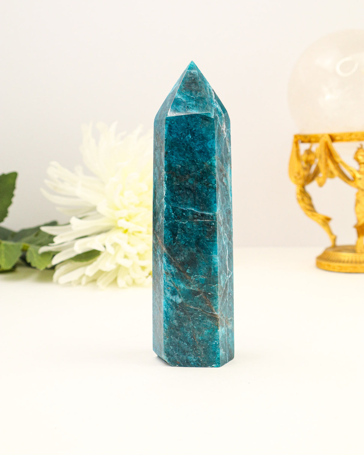 Polished Blue Apatite crystal tower with vibrant ocean-blue colouring photographed on a cream background with floral styling.