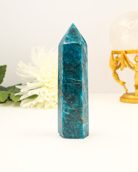 Polished Blue Apatite crystal tower with vibrant ocean-blue colouring photographed on a cream background with floral styling.