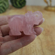 Rose quartz elephant carving displayed on wooden surface beside ruler showing size