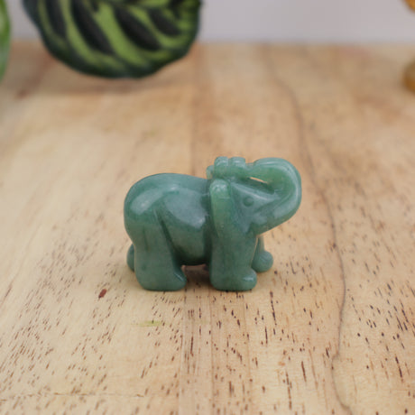 Green aventurine elephant carving displayed on wooden surface beside ruler showing size
