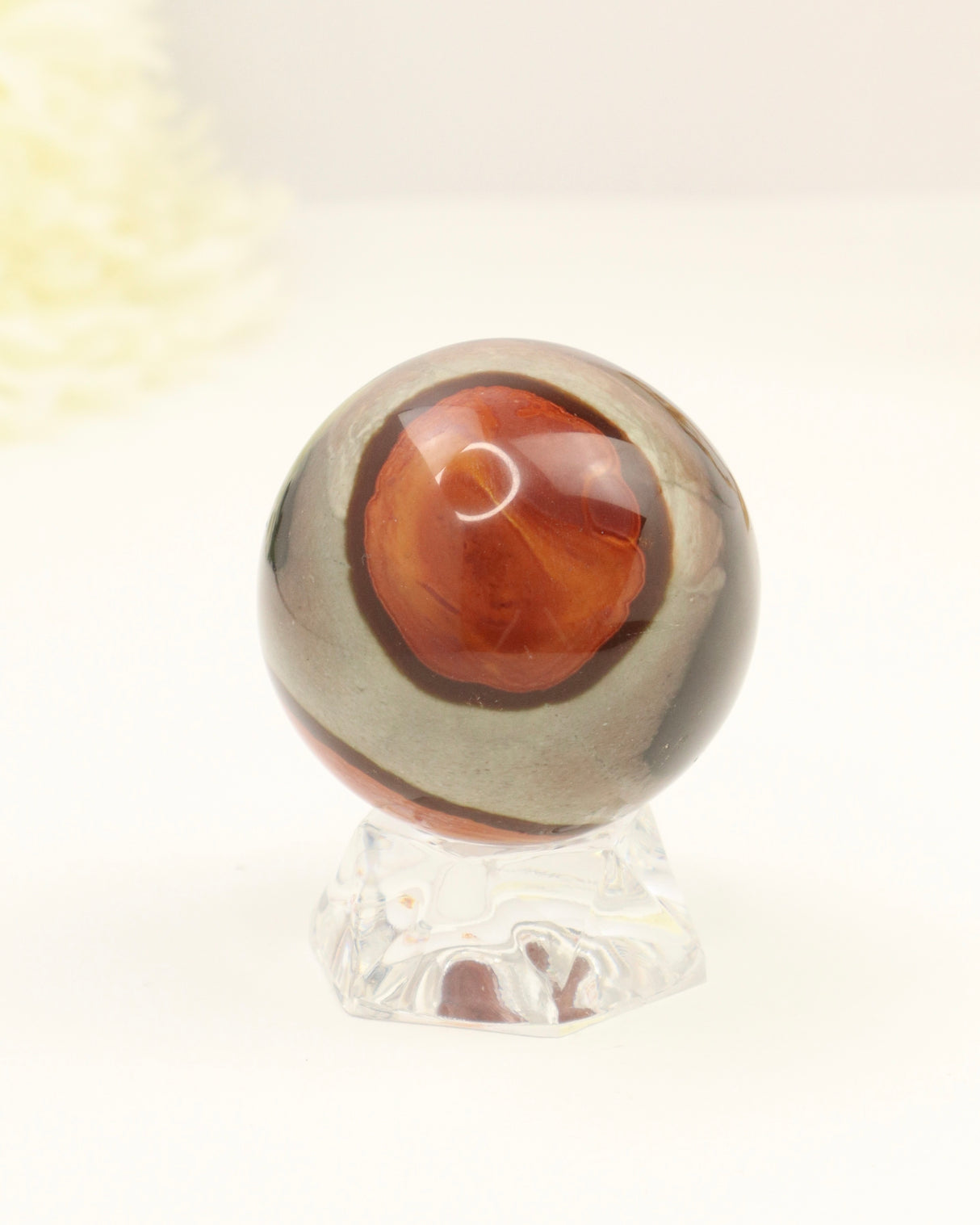 Polished Polychrome Jasper crystal sphere with natural earthy cream, caramel and terracotta patterns displayed on a clear stand against a soft cream background.