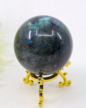 Genuine Labradorite Crystal Sphere 284g featuring vibrant blue labradorescence flashes displayed on a decorative gold stand.