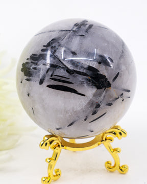 Natural Black Tourmalinated Quartz Crystal Sphere 456g with striking black tourmaline inclusions in polished quartz displayed on a decorative gold stand.