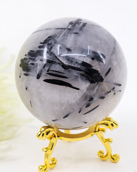 Natural Black Tourmalinated Quartz Crystal Sphere 456g with striking black tourmaline inclusions in polished quartz displayed on a decorative gold stand.