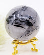 Natural Black Tourmalinated Quartz Crystal Sphere 456g with striking black tourmaline inclusions in polished quartz displayed on a decorative gold stand.