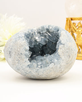 Large polished Celestite geode egg with sparkling pale blue crystal cavity displayed on a cream background.