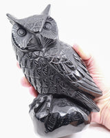Large Black Obsidian Owl Carving 2.418kg held in hand, showing glossy black volcanic glass, detailed feathers, pointed ears and sculpted wings.