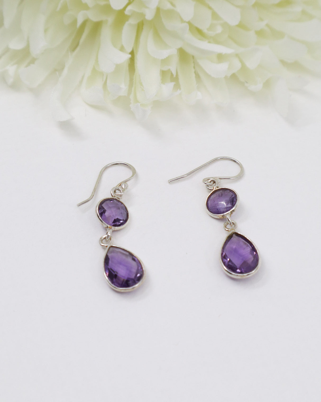 Sterling silver faceted Amethyst drop earrings with elegant teardrop gemstones on white floral background.