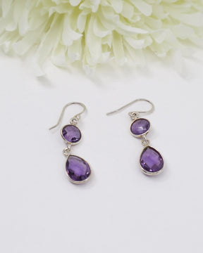 Sterling silver faceted Amethyst drop earrings with elegant teardrop gemstones on white floral background.