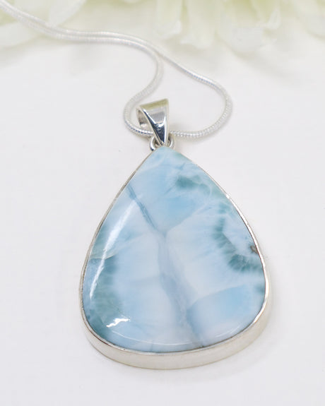 Teardrop-shaped larimar pendant with marbled blue and white design on a beige background