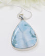 Teardrop-shaped larimar pendant with marbled blue and white design on a beige background
