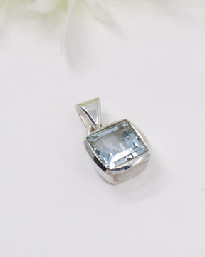 Faceted Blue Topaz sterling silver pendant with sparkling pale blue gemstone in a polished square setting photographed on a white background.