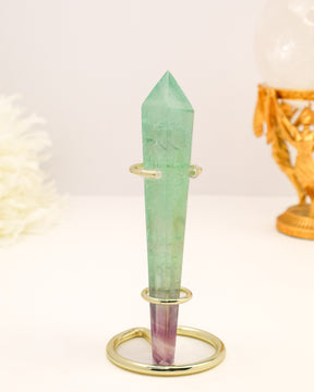 Rainbow Fluorite crystal wand with soft green and purple banding displayed on a gold stand.