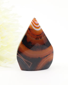 The Ember Gateway Sardonyx Freeform crystal featuring dramatic amber, black and red banding patterns, weighing 139g and measuring 8cm x 5.5cm.